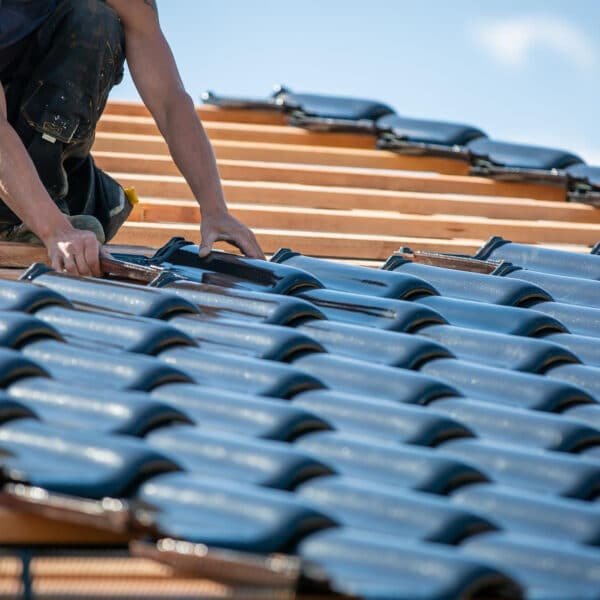 Un homme travaille sur un toit recouvert de tuiles bleues